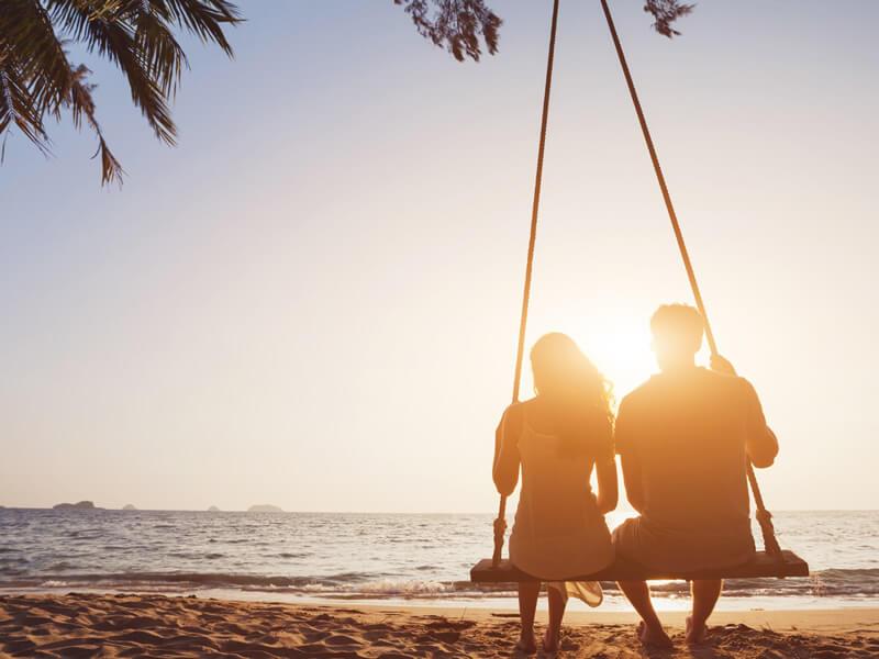 Two people on a swing at sunset on the beach.